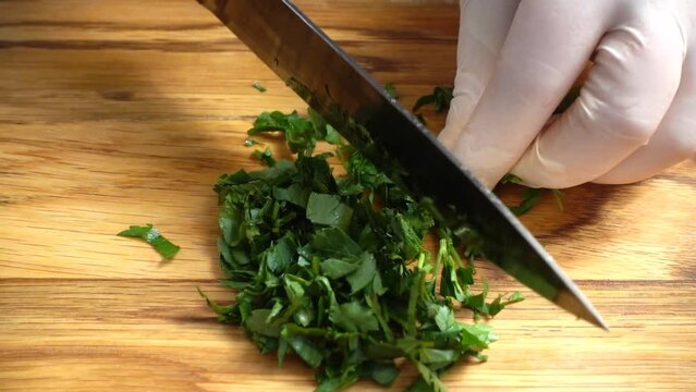 Chef chopping parsley leaves with a knife on a cutting