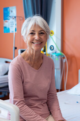 Fototapeta na wymiar Vertical portrait of smiling senior caucasian female patient sitting in hospital, with copy space