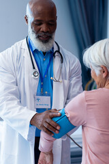 Vertical of happy diverse senior male doctor taking blood pressure of female patient, copy space