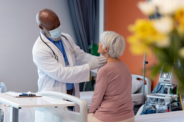 Obraz premium Diverse senior male doctor in face mask examining the throat of senior female patient, copy space