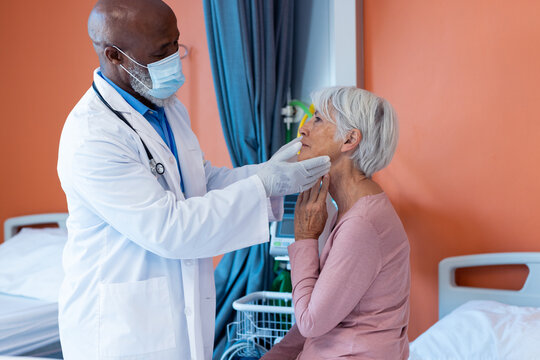 Diverse Senior Male Doctor In Face Mask Examining The Throat Of Senior Female Patient, Copy Space