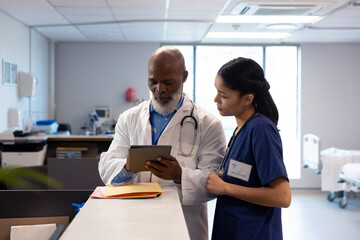 Diverse female and senior male doctor using tablet and talking in hospital ward, copy space