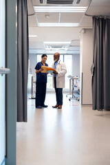 Fototapeta premium Vertical of diverse female and senior male doctor looking at notes, talking in ward, copy space