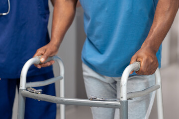 Midsection of doctor and senior african american male patient use walking frame, copy space