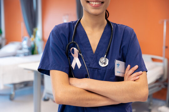 Midsection of smiling biracial female doctor wearing cancer ribbon in hospital ward