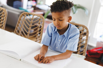 African american blind boy sitting at table, reading braille