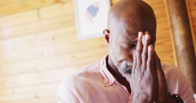 Senior african american man spending time in log cabin and praying, slow motion