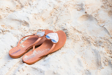 Fototapeta na wymiar Beach flip-flops with shiny heart-shaped decor stand on thebeach