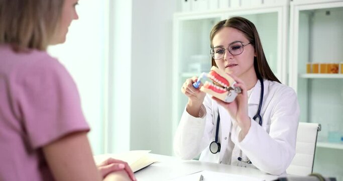 Doctor dentist shows how to properly brush teeth of female patient with dental implants