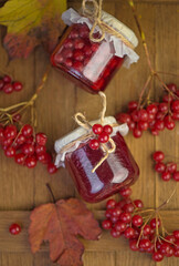 Viburnum fruit jam in a glass jar on a wooden table near the ripe red viburnum berries. Source of natural vitamins. Used in folk medicine. Autumn harvest.