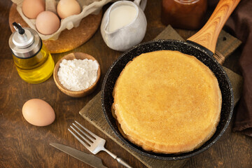 Celebrating Pancake day, cooking healthy breakfast. Delicious homemade crepes or pancakes in a frying pan and ingredients on a rustic table.