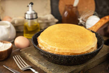 Celebrating Pancake day, cooking healthy breakfast. Delicious homemade crepes or pancakes in a frying pan and ingredients on a rustic table.