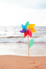 Multi colored plastic pinwheel toy on the beach and against sea and sky. Concept for the summer vacation