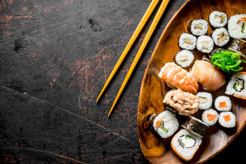Assortment of different types of sushi, rolls and maki on a wooden plate.