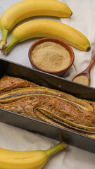 fresh banana bread surrounded by fresh bananas and cooking ingredients lies on a plain gray background close-up. fresh pastries, organic food, vegetarian food