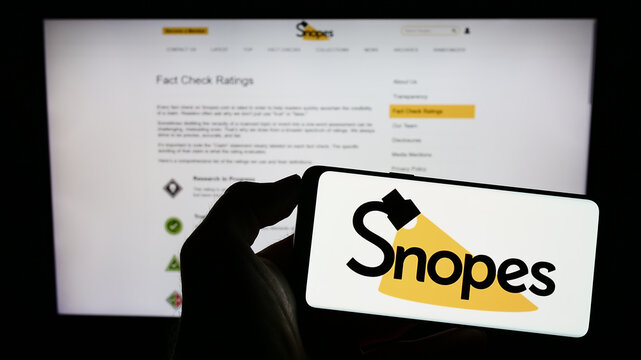 Stuttgart, Germany - 01-14-2023: Person holding cellphone with logo of US fact checking platform Snopes Media Group Inc. on screen in front of webpage. Focus on phone display.