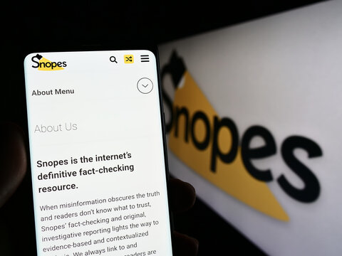 Stuttgart, Germany - 01-14-2023: Person holding cellphone with website of US fact checking platform Snopes Media Group Inc. on screen with logo. Focus on center of phone display.