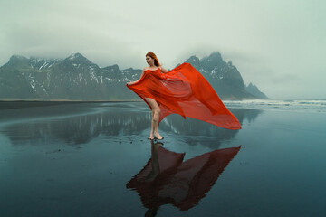Attractive model in red dress on Reynisfjara beach scenic photography. Picture of person with hills on background. High quality wallpaper. Photo concept for ads, travel blog, magazine, article
