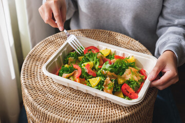 Closeup image of a woman eating salad in paper box for takeaway food at home