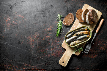 Sprats in a tin with bread and rosemary on the cutting Board.