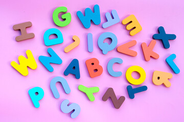 Colorful wooden alphabets on pink background.
