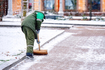 Street cleaner man clear snow from sidewalk, cleans footpath from snow during blizzard. Utility worker shoveling snow on city street. Janitor clearing snowy walkway with shovel..