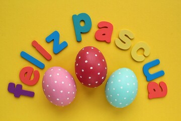 Feliz Pascua, Happy Easter letters on spanish and color eggs on yellow background. Holiday banner, flatlay creative composition. Greeting card, poster, banner, web. Top view festive concept. Flat lay