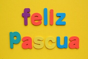 Feliz Pascua, Happy Easter on spanish colored lettering on yellow background. Holiday spring compostion concept. Creative idea for greeting card, poster, banner, invitation. Top view, flat lay