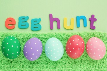 Egg hunt letters on green background and coloured eggs with polka dot on spring grass background. Easter greeting card, invitation, banner, poster sale. Flatlay, top view holiday concept. Sign for fun