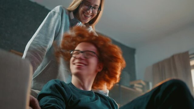 Red haired teenager shakes his hair while spending free time with his sister in the room at home