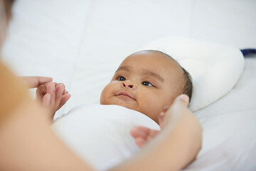 African baby girl learning to walk and mother or sitter holding hands on bedroom