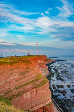 View over red sandstone cliffs in island Helgoland at Northern Sea with rich marine wildlife, radio communication towers and modern lighthouse, Germany, summer, sunset colors.