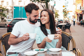 Smiling beautiful woman and her handsome boyfriend. Happy cheerful family. Couple drinking coffee in restaurant. They drinking tea at cafe in street. Holding cup. Enjoying their date. Hugging, kiss