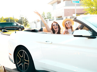 Portrait of two young beautiful and smiling hipster female in convertible car. Sexy carefree women...