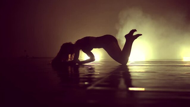 Silhouette woman in sensual performance moves on a stage with spotlight and smoke in the background