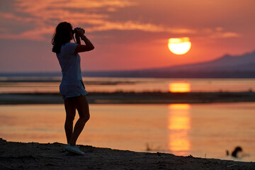 On safari in Zimbabwe: Silhouette of a Fit Woman standing on the Banks of the Zambezi River,...