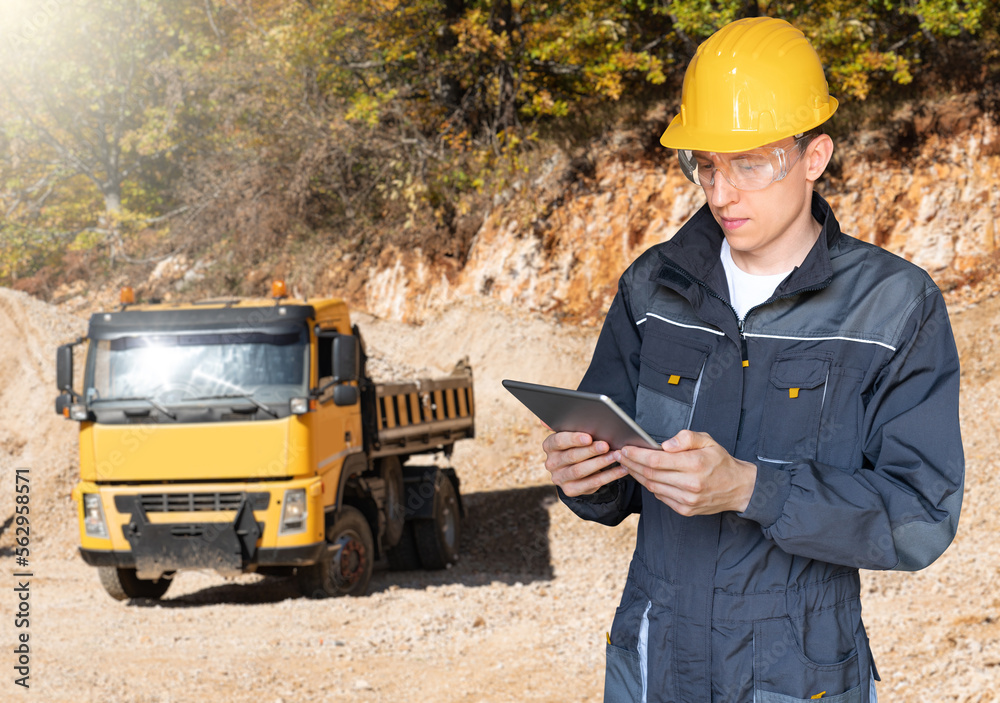 Poster engineer in a helmet with a digital tablet on the background of construction machine