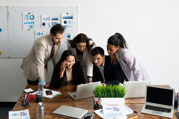 Business people stand in the office, bending over a laptop, waiting for the outcome of the transaction.