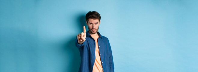 Serious young man extend one finger to stop or warn you, prohibit something or disapprove, standing...