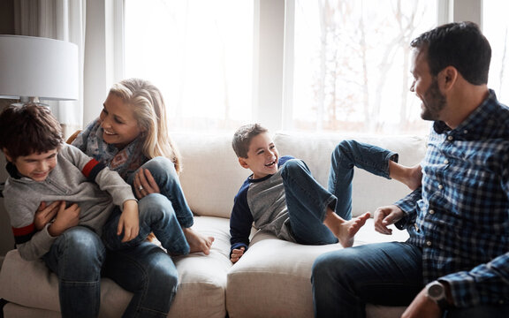Love, bonding and family on the sofa for fun, playing and playful energy in their house. Relax, happy and parents with crazy children to play wrestle on the couch during quality time in a home