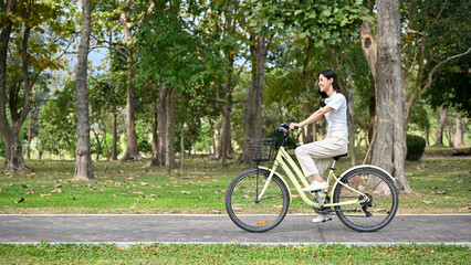 Chilling and relaxed young Asian woman riding a bicycle on the bike lane in the park.