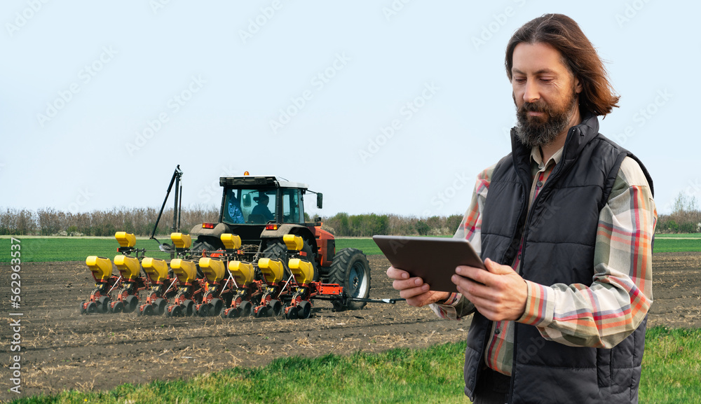 Poster farmer with a digital tablet on the background of an agricultural tractor with seeding machine