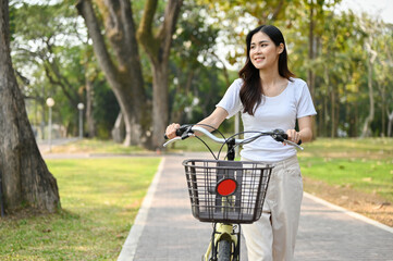 Chill Asian woman walking along the sidewalk with her bicycle in the beautiful nature park.