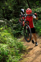 Woman cyclist carry a mountain bike walking on tropical forest trail
