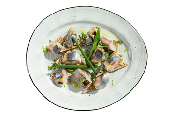 Pieces of salted herring with green onions on a plate. Appetizing traditional snack. Close-up. Isolated on a white background.