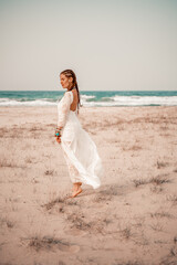 Fototapeta na wymiar Model in boho style in a white long dress and silver jewelry on the beach. Her hair is braided, and there are many bracelets on her arms.