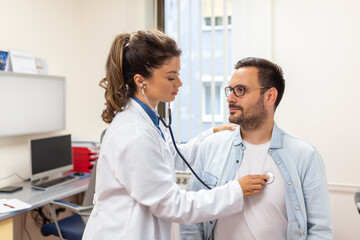 Caring Caucasian female doctor use phonendoscope examine male patient heart rate at consultation in...