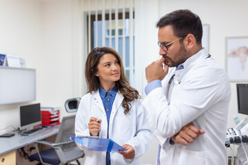 Fototapeta premium Doctors discussing over a medical report in hospital. Female and male doctor checking clinical report of patient online. Healthcare staff having discussion in a office of private clinic.