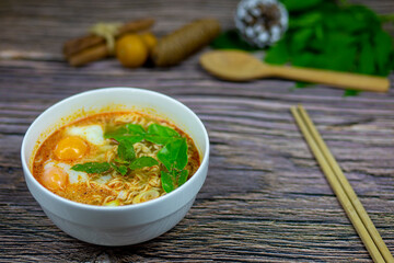 This lunch is instant noodles Tom Yum Kung flavour herbs onsen eggs served on wooden table.