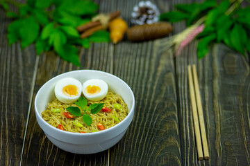 Noodles with Boiled Eggs topping chilli and basil come to serving on dark wood table is my lunch for this meal.